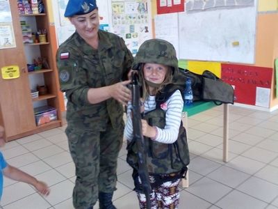 Grafika przedstawia panią żołnierz i wychowankę Placówki Wsparcia Dziennego w Laskach w ubiorze wojskowym. 