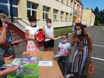 Zdjęcie przedstawia wychowawczynie z przedszkola w Ostrowcu wręczającą upominki wychowance, a także jej opiekunkę. 