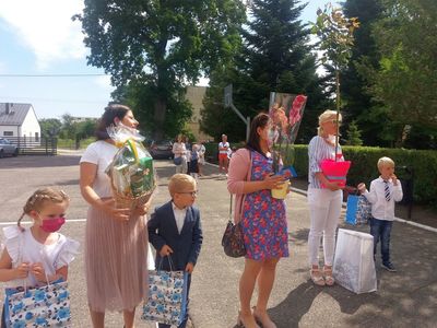 Zdjęcie przedstawia rodziców i dzieci z kwiatami oraz upominkami. 