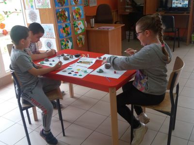 Zdjęcie ukazuje trzech wychowanków Placówki Wsparcia Dziennego w Laskach malujących kamienie.