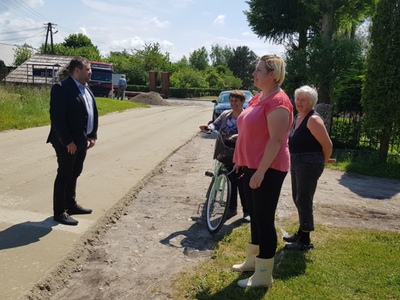 Zdjęcie przedstawia wójta Radosława Nowakowskiego podczas rozmowy z sołtys i mieszkankami Bartolina w miejscu remontowanej drogi gminnej. 