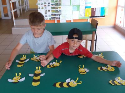 Zdjęcie przedstawia dwóch wychowanków Placówki Wsparcia Dziennego w Laskach eksponujących wykonane pszczoły z papieru. 
