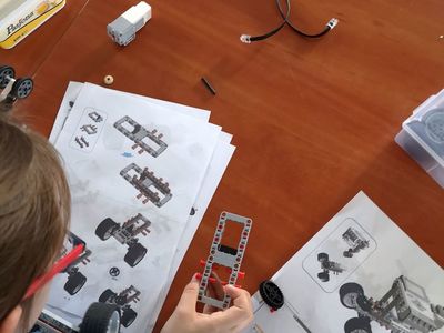 Zdjęcie przedstawia części do złożenia robota wraz z instrukcją i głowę wychowanki Placówki Wsparcia Dziennego w Pękaninie, pracującego nad zbudowaniem robota.