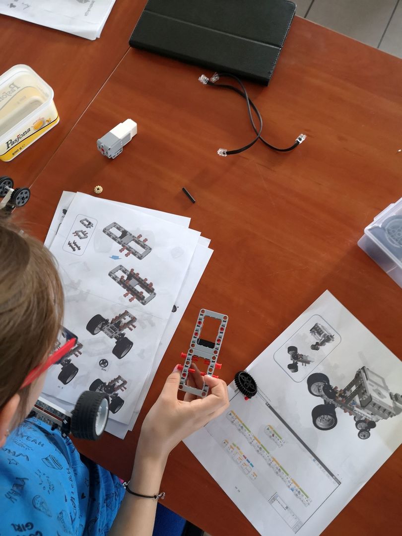 Zdjęcie przedstawia części do złożenia robota wraz z instrukcją i głowę wychowanki Placówki Wsparcia Dziennego w Pękaninie, pracującego nad zbudowaniem robota.