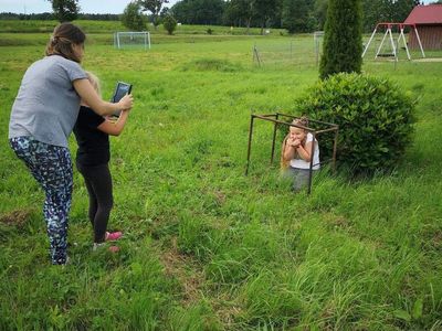 Zdjęcie przedstawia wychowanków Placówki Wsparcia Dziennego w Kusicach: dziewczynkę pozującą do zdjęcia oraz inną osobę wykonującą fotografię przy pomocy wychowawcy.  