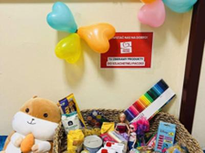 Zdjęcie przedstawia zebrane produkty leżące w koszu nad nim plakat szlachetnej paczki, obok wiszą balony.