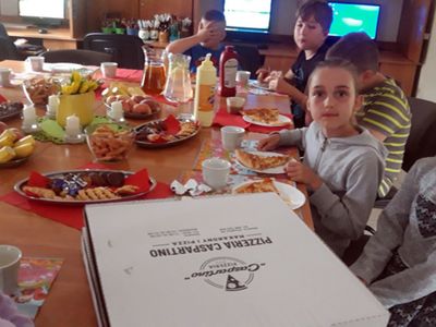 Zdjęcie przedstawia wychowanków Placówki Wsparcia Dziennego z Kosierzewa jedzących pizzę przy stole w świetlicy.