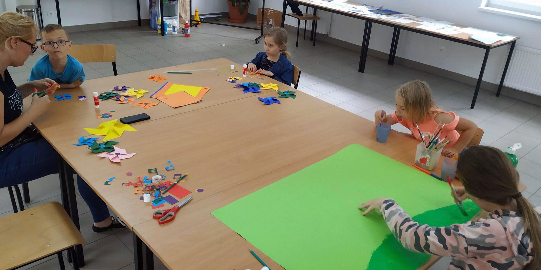 Zdjęcie przedstawia wychowanków Placówki Wsparcia Dziennego z Gorzycy oraz mamę jednego z dzieci, którzy przygotowują wspólnie  kolorowe wiatraki w świetlicy. 
