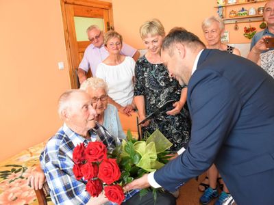 Zdjęcie przedstawia wójta Radosława Nowakowskiego wręczającego kwiaty na ręce Jubilata Stanisława Filipiaka z Pękanina. W tle rodzinka Jubilata. 