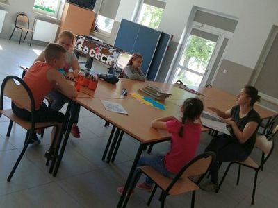 Zdjęcie przedstawia wychowanków Placówki Wsparcia Dziennego z Kusic z wychowawczynią przy stolikach.