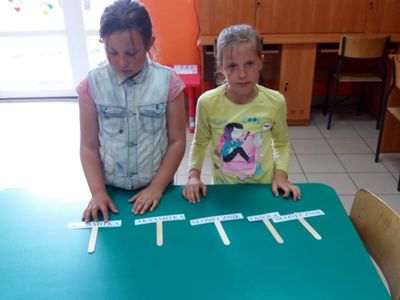Zdjęcie przedstawia wychowanki Placówki Wsparcia Dziennego z Lasek w świetlicy, które prezentują przygotowane napisy z nazwami roślin.