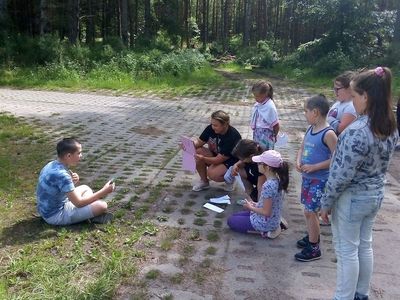 Zdjęcie przedstawia wychowanków Placówki Wsparcia Dziennego z Lasek podczas zajęć teatralno - dziennikarskich, które odbywały się na dworze.