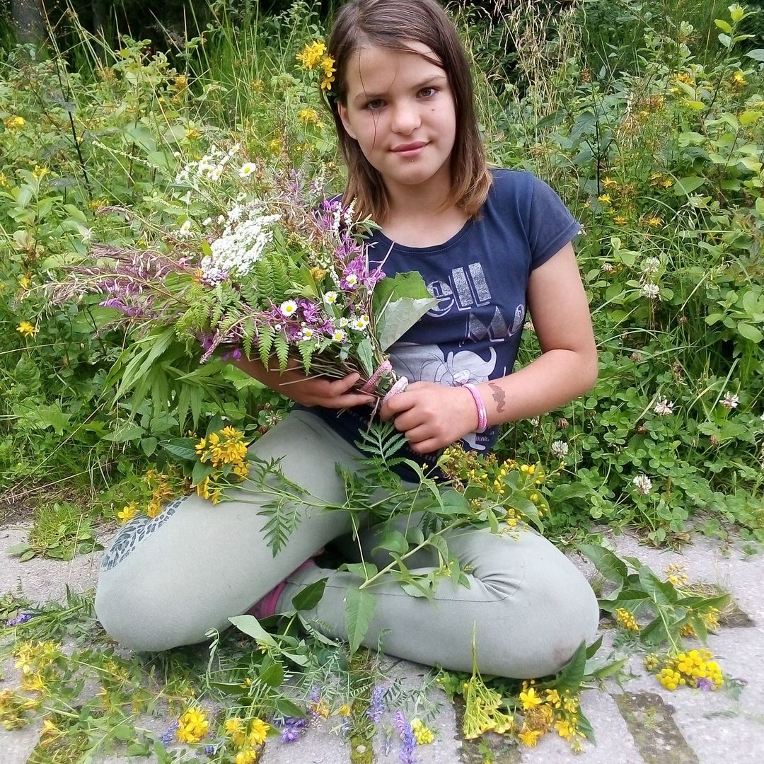 Zdjęcie przedstawia dziewczynkę z PWD z Lasek na tle kwiatów w lesie.