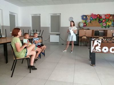 Zdjęcie przedstawia wychowawce prowadzącą zajęcia teatralno-dziennikarskie oraz obserwujące ją dzieci z Placówki Wsparcia Dziennego w Kusicach.