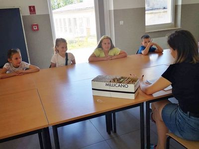 Zdjęcie przedstawia dzieci uczestniczące w  zajęciach pt. Jak odczytać czas w Placówce Wsparcia Dziennego w Kusicach oraz wychowawczynię.