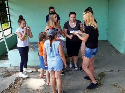 Zdjęcie przedstawia wychowanków Placówki Wsparcia Dziennego z Paprot  z wychowawcą podczas przygotowania do zadania sprawnościowego - kto najszybciej przeniesie łyżkę mąki.