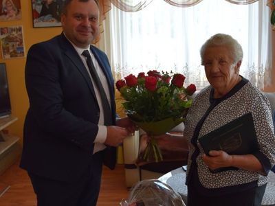 Zdjęcie przedstawia wójta Radosława Nowakowskiego i Panią Marię Musielaniec, który wręcza bukiet kwiatów Jubilatce. 