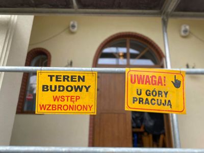 Zdjęcie przedstawia tabliczkę z napisem Teren Budowy Wstęp Wzbroniony oraz Uwaga! U góry pracują, które znajdują się przed modernizowanym domem przedpogrzebowym w Malechowie. 