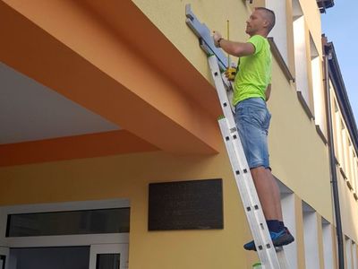 Zdjęcie przedstawia montaż napisu Świetlica Kultury w Malechowie, mężczyznę na drabinie podczas prac montażowych. 