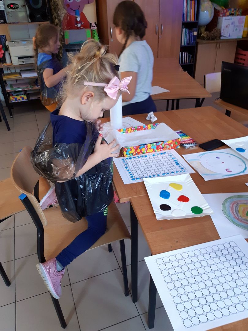 Zdjęcie przedstawia dziewczynkę podczas malowania paluszkami i farbami oraz pozostałe podopieczne PWD Paproty w tle.