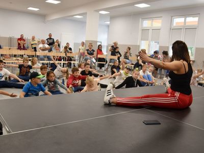Zdjęcie przedstawia zajęcia pokazowe breakdance w Świetlicy Kultury w Malechowie: instruktorkę oraz dzieci biorące udział w lekcji pokazowej.