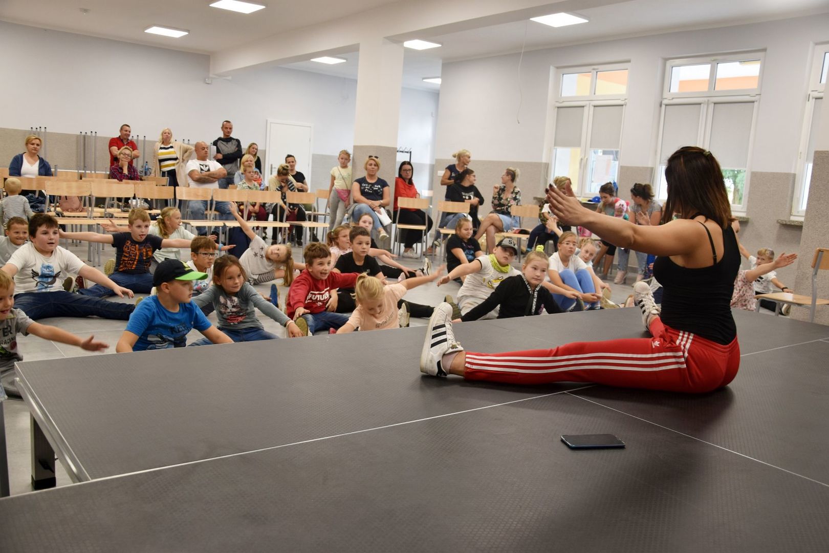 Zdjęcie przedstawia zajęcia pokazowe breakdance w Świetlicy Kultury w Malechowie: instruktorkę oraz dzieci biorące udział w lekcji pokazowej.