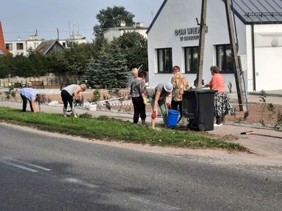 Zdjęcie przedstawia panie z Klubu Seniora w Ostrowcu sprzątające teren przy Domu Wiejskim w Ostrowcu. 