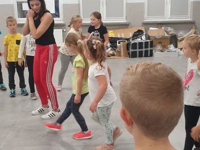 Zdjęcie przedstawia dzieci uczestniczące w zajęciach breakdance w Świetlicy Kultury w Malechowie wraz z instruktorką, która uczy je poszczególnych kroków. 