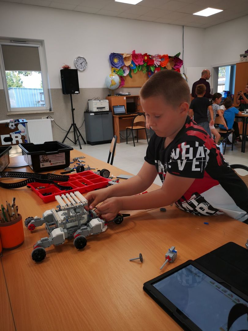 Zdjęcie przedstawia chłopca podczas konstrukcji robota podczas zajęć robotyki w PWD Kusice.