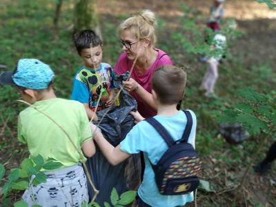 Zdjęcie przedstawia dzieci wraz z wychowawczynią wynoszące duży worek na drogę.
