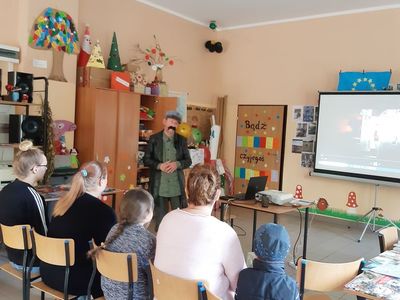 Zdjęcie przedstawia uczestników lekcji bibliotecznej w świetlicy w Paprotach oraz prowadzącego przebranego w strój marszałka Piłsudskiego.