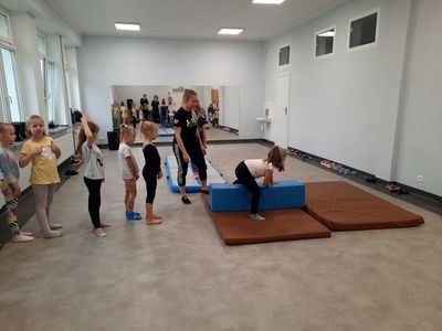 Zdjęcie przestawia dzieci uczestniczące w zajęciach akrobatyki i tańca z trenerką, podczas wykonywania ćwiczenia w sali tanecznej Świetlicy Kultury w Malechowie.