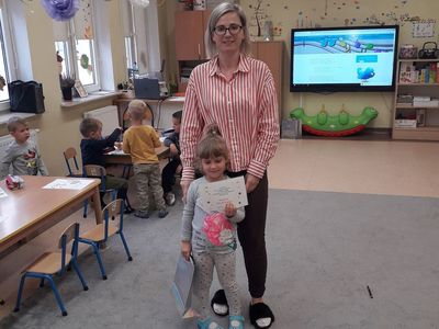Organizator konkursu Marta Wiącek z nagrodzoną dziewczynką, w tle przedszkolaki.