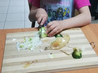Zdjęcie przedstawia dziewczynkę z PWD w Sulechowie podczas krojenia warzyw.