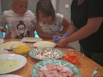 Zdjęcie przedstawia wychowawcę i dzieci podczas wykonywania pizzerek.