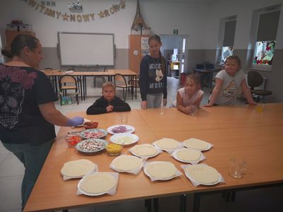 Zdjęcie przedstawia wychowawcę i grupe dzieci podczas warsztatów kulinarnych.