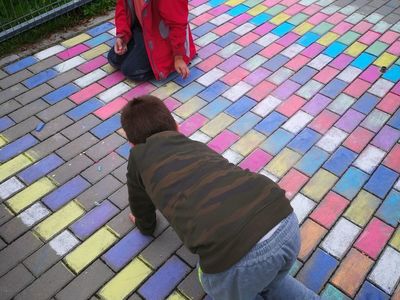 Dzieci z Placówki Wsparcia Dziennego w Kusicach podczas malowania kredą kostki polbrukowej. 