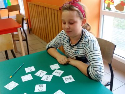Dziecko z PWD Laski grające w grę polegającą na odnalezieniu par zegarów analogowy - elektroniczny, wskazujących tę samą godzinę.