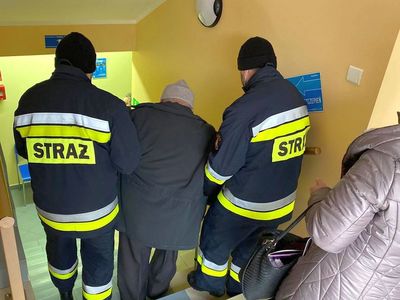 Strażacy pomagają seniorowi w przejściu do punktu szczepień. 