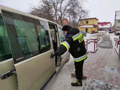 Strażak z OSP Malechowo pomaga seniorce wysiąść z auta. 