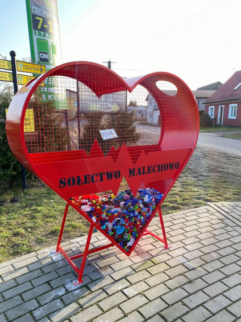 Czerwony pojemnik na nakrętki z napisem Sołectwo Malechowo. 