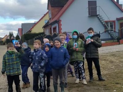 Grupa dzieci, która pokazuje wykonane przez siebie laurki dla kobiet.