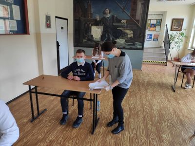 Nauczycielka z Zespołu Szkół w Ostrowcu przekazuje uczniom arkusze egzaminacyjne. 