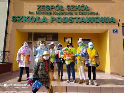 Grupa uczniów z Zespołu Szkolnego w Ostrowcu przed budynkiem szkoły gotowa do powitania wiosny.