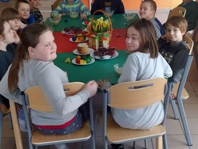 Wychowankowie z Placówki Wsparcia Dziennego w Laskach, siedzący przy stolikach, na których znajdują się dekoracje wielkanocne.
