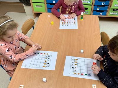 4-latki podczas wykonywania ćwiczenia z piktogramami - łączenie cech. Trójka dzieci przy stoliku pracuje z przygotowanymi materiałami. 