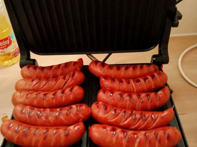 Kiełbaski pieką się na grillu elektrycznym. 