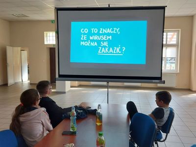 Projekcja filmu na temat wirusów, dzieci z Placówki Wsparcia Dziennego w Pękaninie oglądają informacje wyświetlone na ekranie w sali głównej świetlicy. 