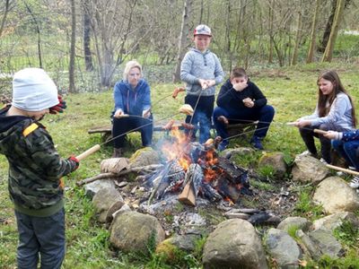 Dzieci z Placówki Wsparcia Dziennego w Kosierzewie po wykonanej pracy, przy ognisku zajadają się kiełbaskami.