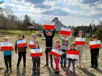 Wychowankowie Placówki Wsparcia Dziennego w Sulechowie przed świetlicą, pozują z własnoręcznie wykonanymi flagami.
